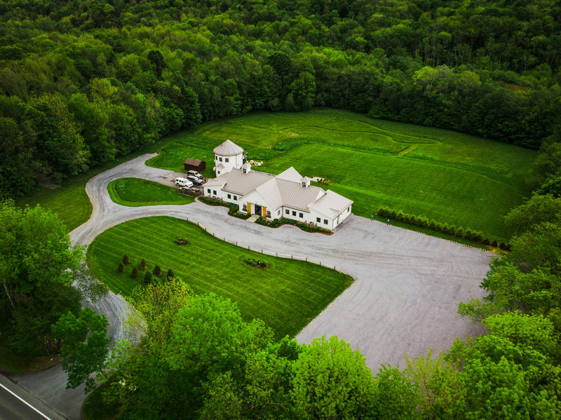 Aerial view of an event venue's driveway and lawn beneath forested hills