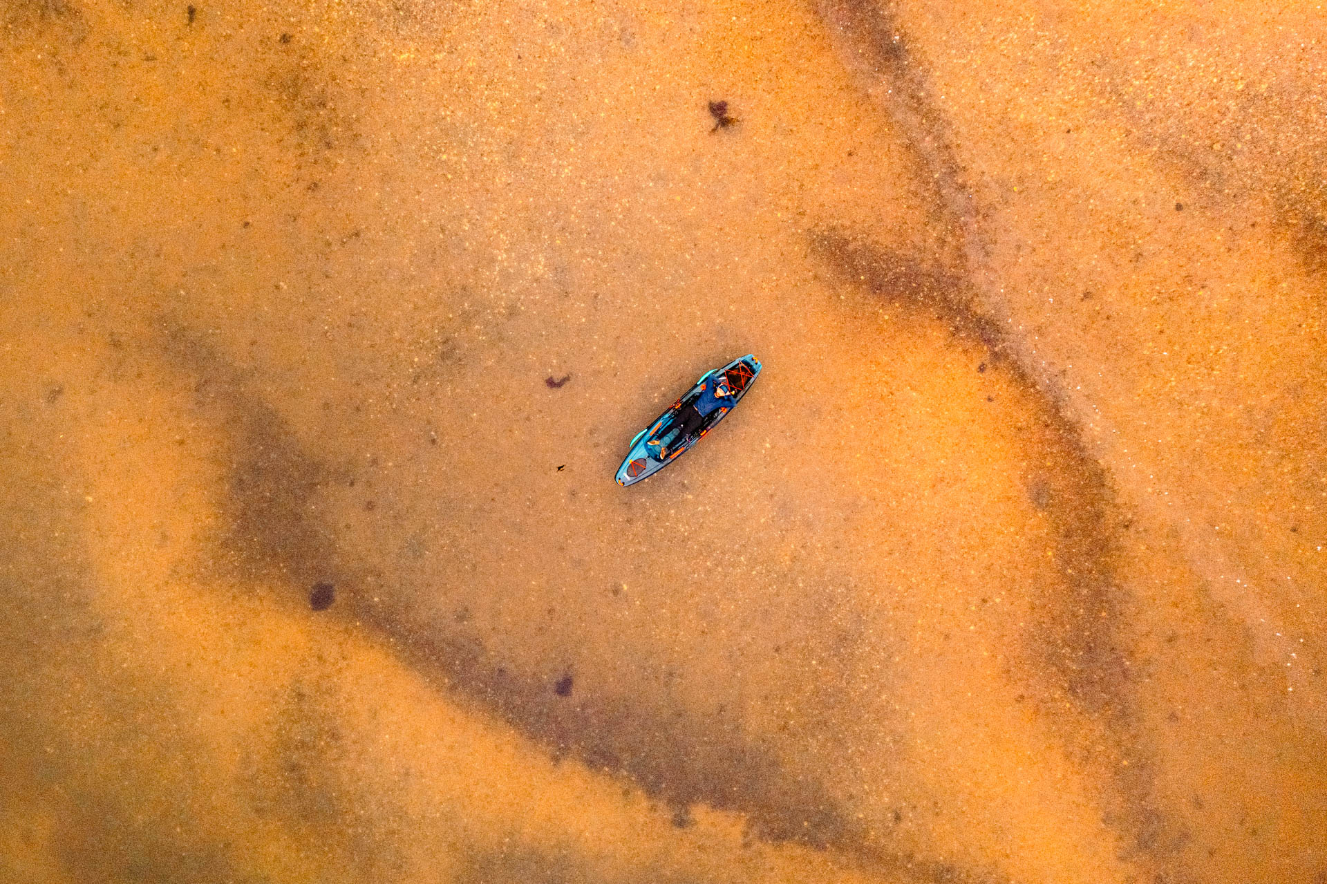 Kayak crossing rust-colored water, aerial view